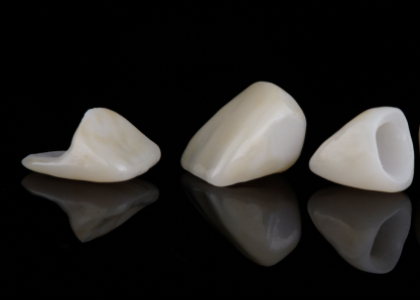 Three dental crowns made of ceramic, showcasing various shapes and angles, reflecting light against a black background, illustrating options for restorative dentistry at Citrus Smiles Dental Studio.