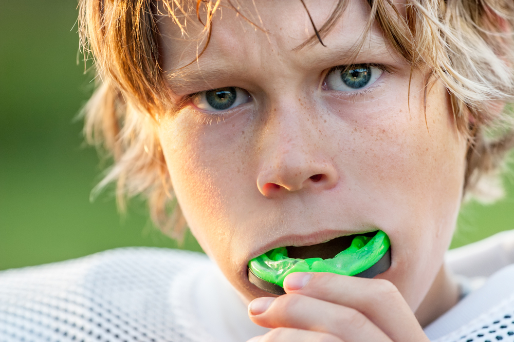 Young athlete with green sports mouth guard, emphasizing dental protection for sports, in context of personalized mouth guard services at Citrus Smiles Dental Studio.