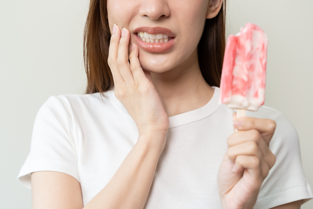 Face,Expression,Suffering,From,Sensitive,Teeth,,Asian,Young,Woman,Touching Woman experiencing tooth sensitivity while holding a popsicle, illustrating post-whitening discomfort and sensitivity management tips.