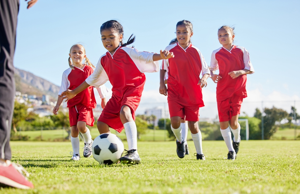 Girls in red soccer uniforms playing on a field, demonstrating teamwork and athleticism during a recreational sports activity.