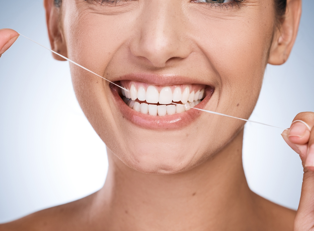 Smiling woman using dental floss to maintain oral hygiene, emphasizing the importance of teeth whitening and healthy habits at Citrus Smiles Dental Studio.